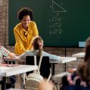 Happy black elementary school teacher taking to her students in